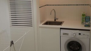 A compact laundry area with a washing machine, a sink, and a drying rack.