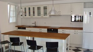 A modern kitchen with white cabinets, a wooden countertop, and a black and white checkered floor. There are three black bar stools and two pendant lights.