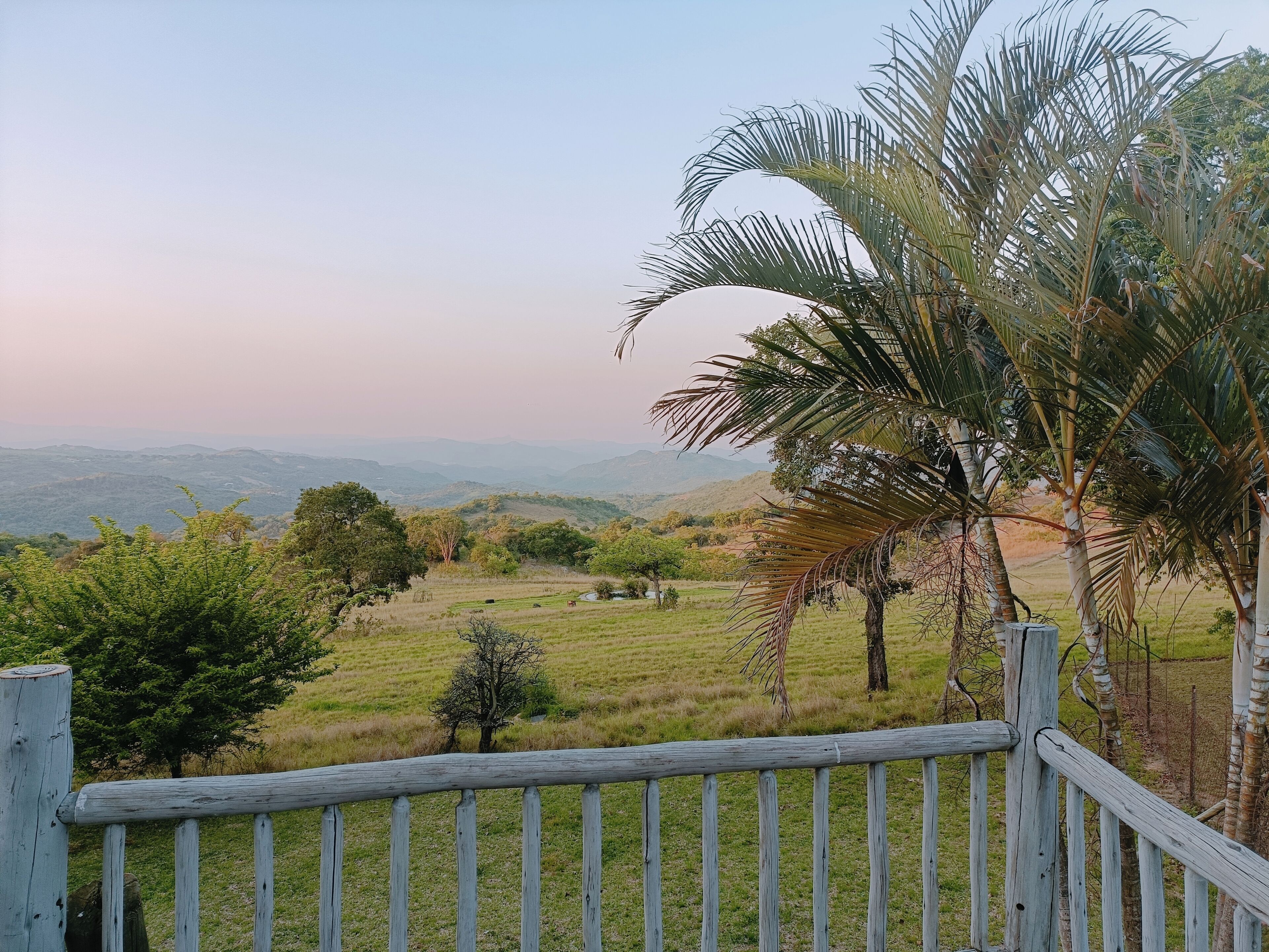 A scenic view from a wooden deck overlooking a grassy landscape with trees and distant hills.