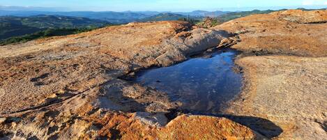 A rocky landscape with a small water body and distant hills.