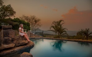 A person sitting on a rock by a pool with a view of mountains and trees.