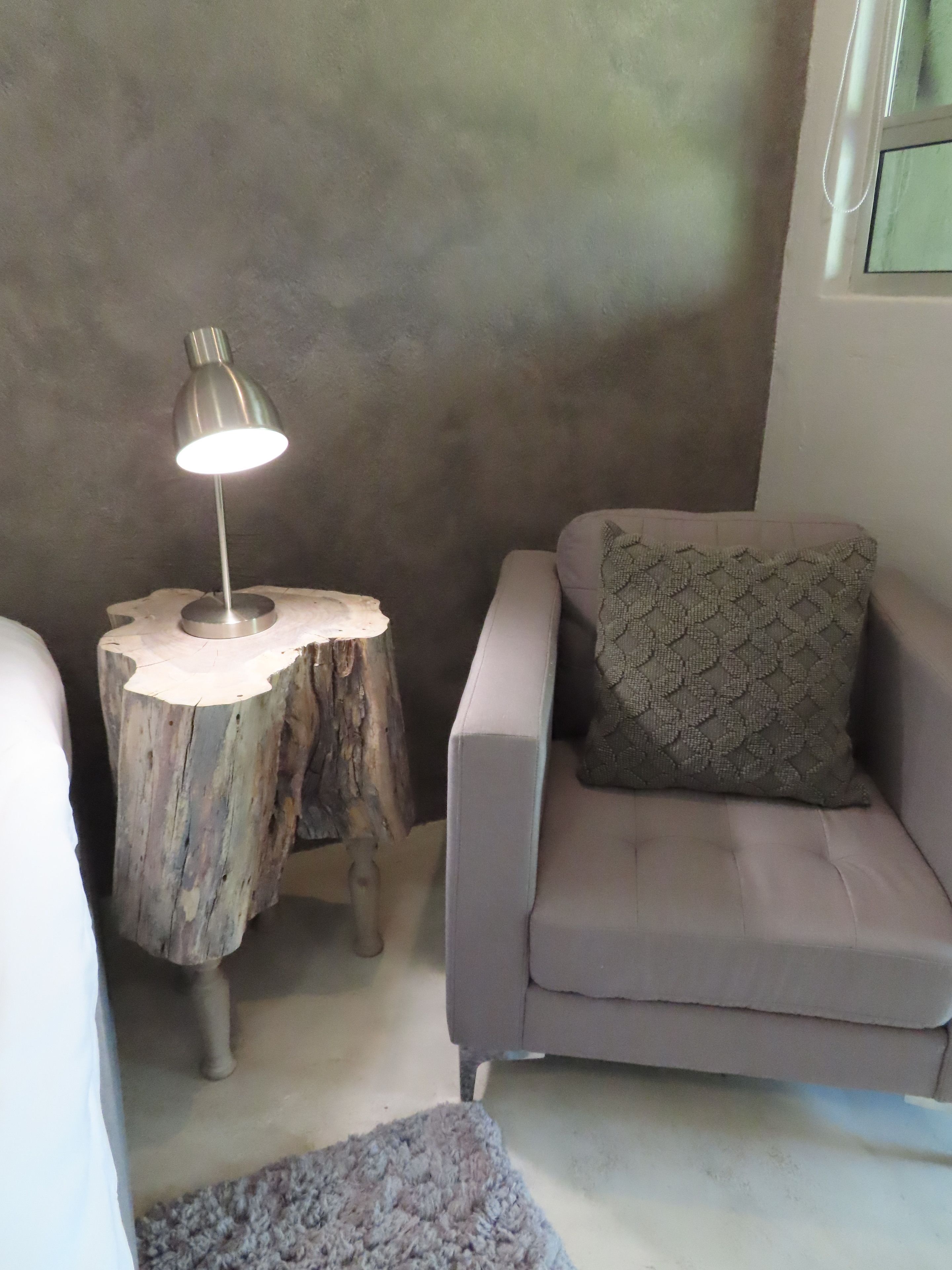 Una habitación acogedora con un sofá gris, una mesita redonda de madera con una lámpara y un cojín estampado.