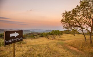A walking trail sign in a natural landscape with trees and distant hills.