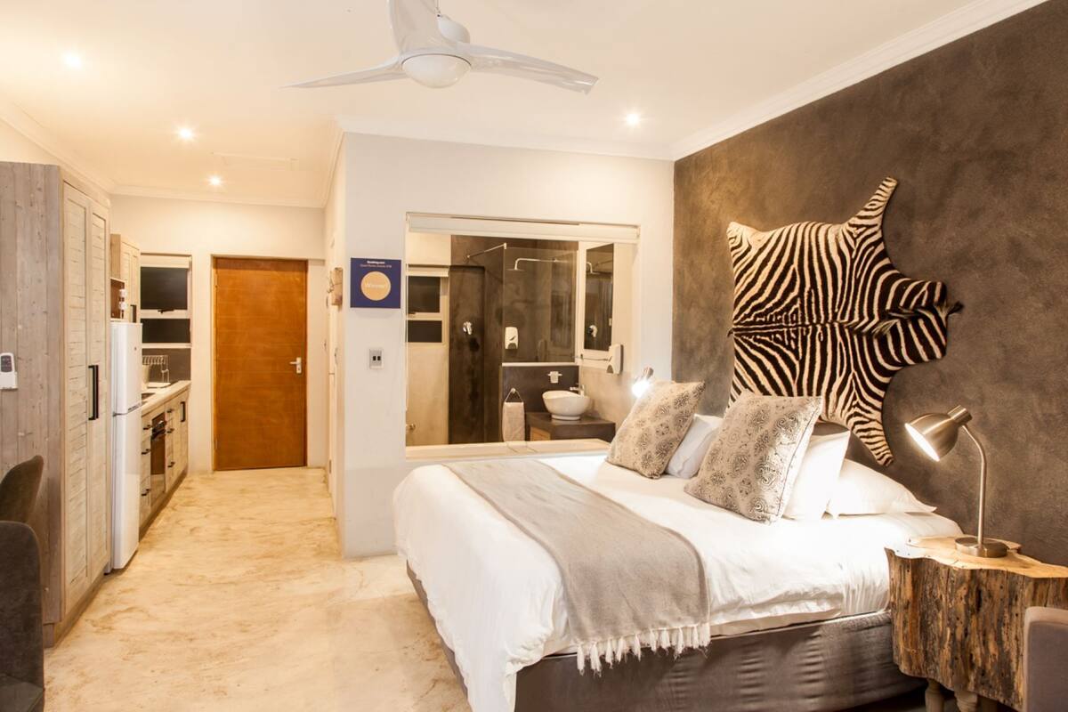 A modern bedroom with a large bed, a zebra-patterned wall decoration, a wooden bedside table, and a ceiling fan.