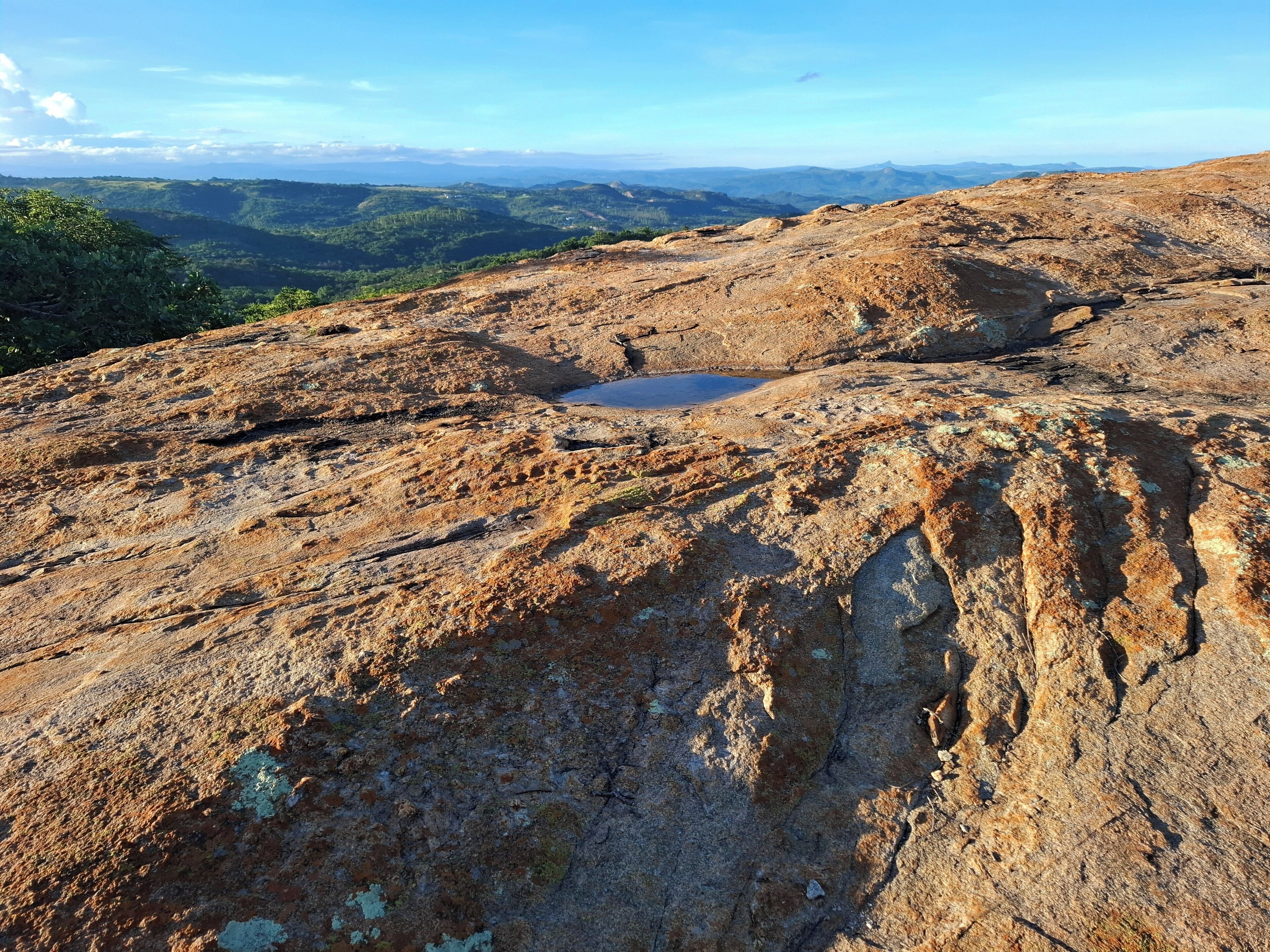 A rocky landscape with a small water body and distant green hills.