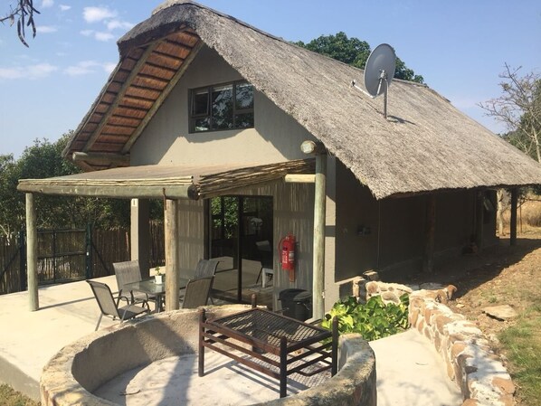 A thatched-roof house with a covered patio, outdoor seating, and a fire extinguisher.