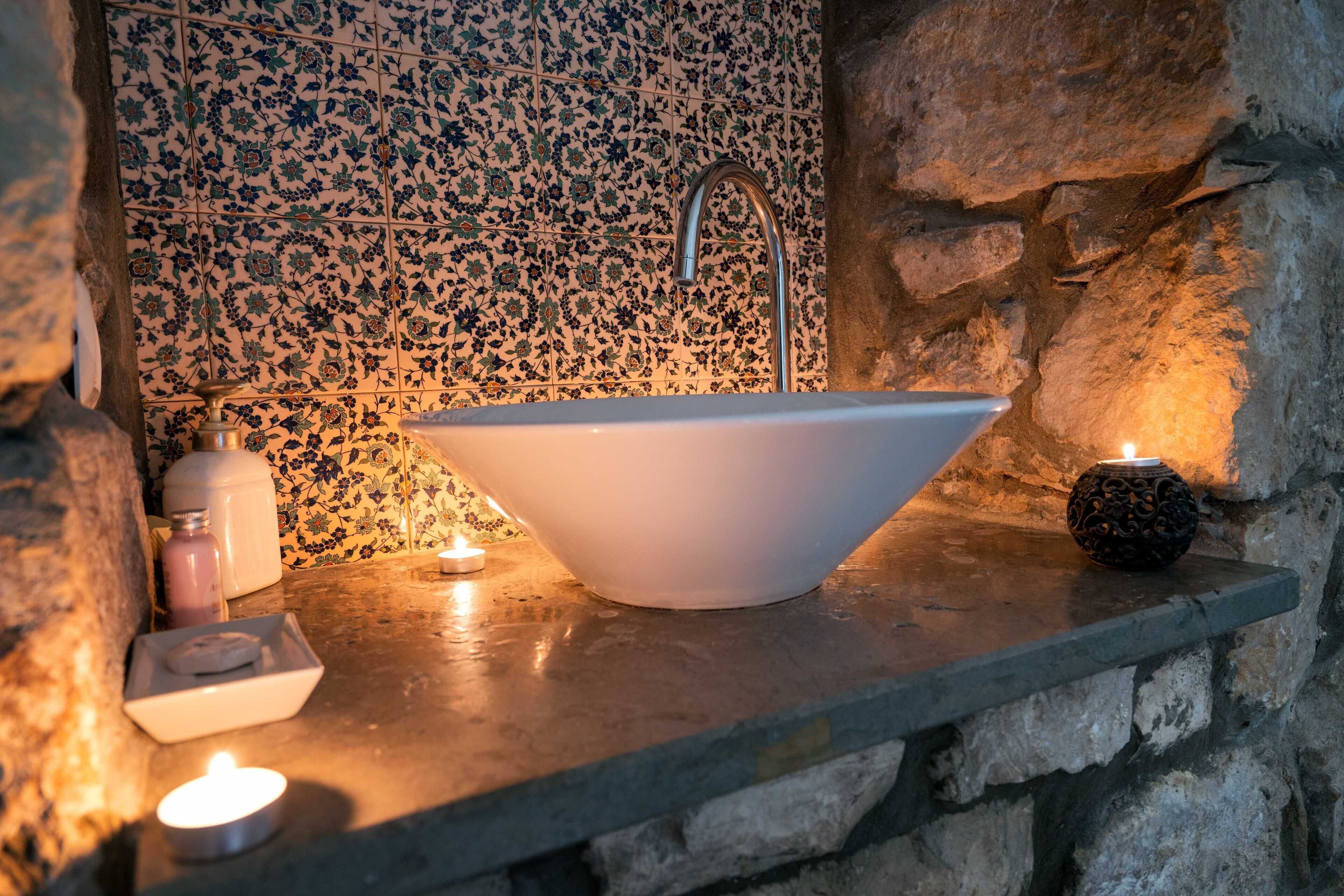 A bathroom with a freestanding white sink, a stone wall, and a tiled backsplash.