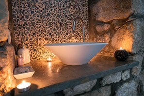A bathroom with a freestanding white sink, a stone wall, and a tiled backsplash.
