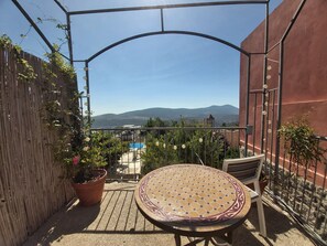 Une terrasse avec une table et des chaises, une clôture en bois et une vue sur des montagnes lointaines.