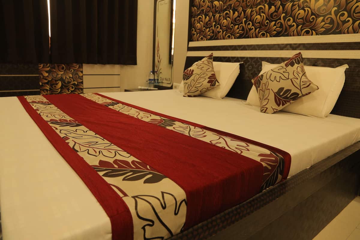 A hotel room with a neatly made bed, a red and white patterned bedspread, and a decorative headboard.