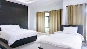 Habitación de hotel con dos camas, cabecera oscura, ventana con cortinas y pared blanca.