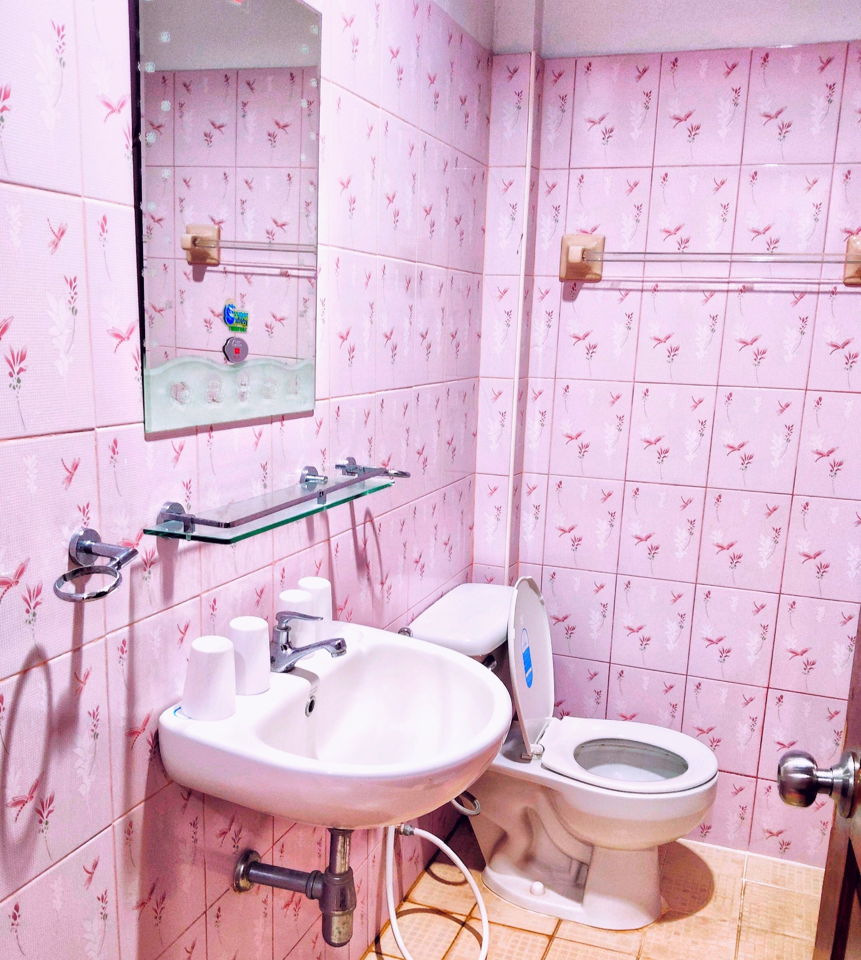 Un baño con baldosas rosa con motivos florales, un lavamanos blanco con un espejo encima y un inodoro con un adhesivo azul.