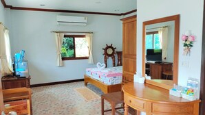 A bedroom with a bed, a wooden dresser, a desk, a mirror, an air conditioner, a window with curtains, a clock, and a television. - Nahinlad Resort (Pak Phli)