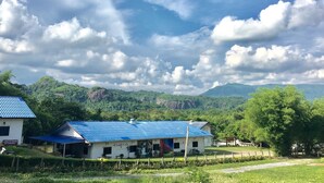 A rural house with a blue roof, surrounded by lush greenery and mountains in the background. - Nahinlad Resort (Pak Phli)