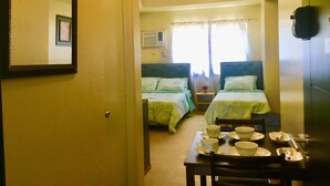 A room with two beds, a dining table with bowls and cups, and a mirror on the wall. - Davao Avida Towers by JYU (Davao)