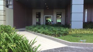 A building entrance with a covered walkway, a security guard, and a landscaped area with plants. - Davao Avida Towers by JYU (Davao)