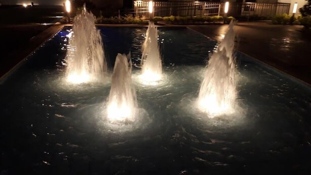 A nighttime view of a swimming pool with multiple water jets. - Davao Avida Towers by JYU (Davao)