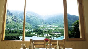 A dining table set for four with a view of a mountainous landscape through large windows. - Primo Resorts (Manali)