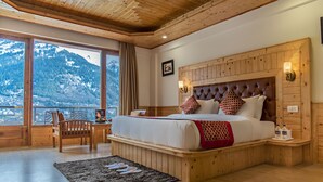 A bedroom with a large bed, wooden headboard, and a view of mountains through a window. - Primo Resorts (Manali)