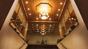 Una escalera con escalones de madera y un candelabro, que conduce a una habitación con un espejo grande y plantas en macetas.