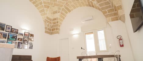 Une pièce avec un plafond en pierre, un canapé marron, une table à manger avec des chaises et un mur orné de tableaux.