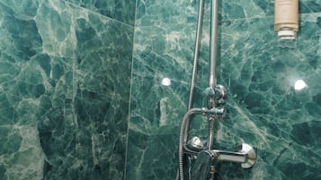 Un baño con ducha, cabezal de ducha de mano y una botella de champú.