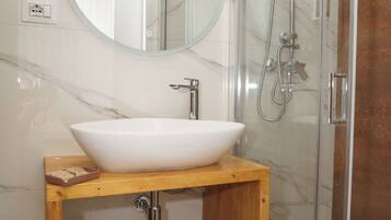 A bathroom with a white marble sink, a wooden vanity, a round mirror, and a glass-enclosed shower.