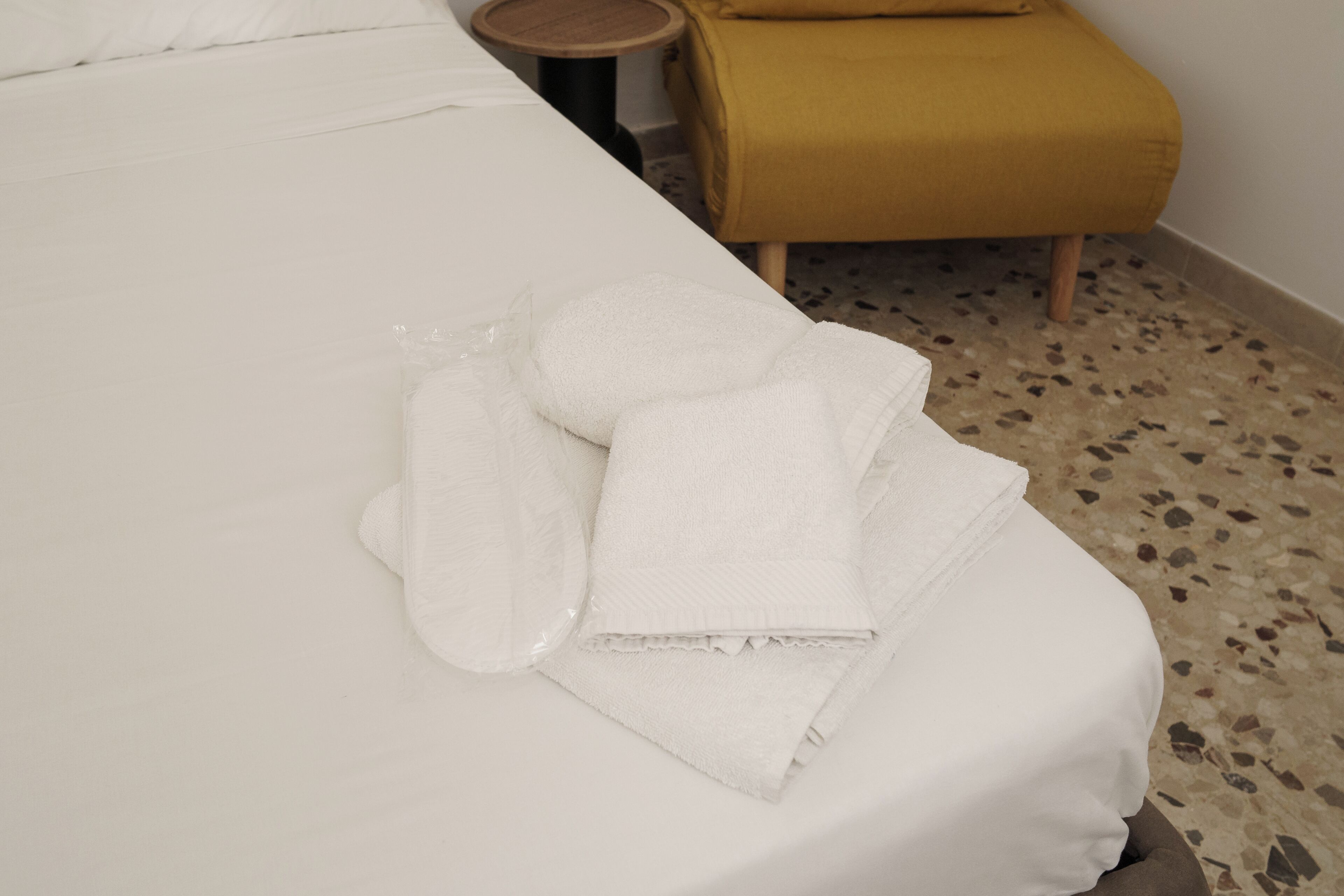 A neatly made bed with white linens and a rolled-up towel on the side.