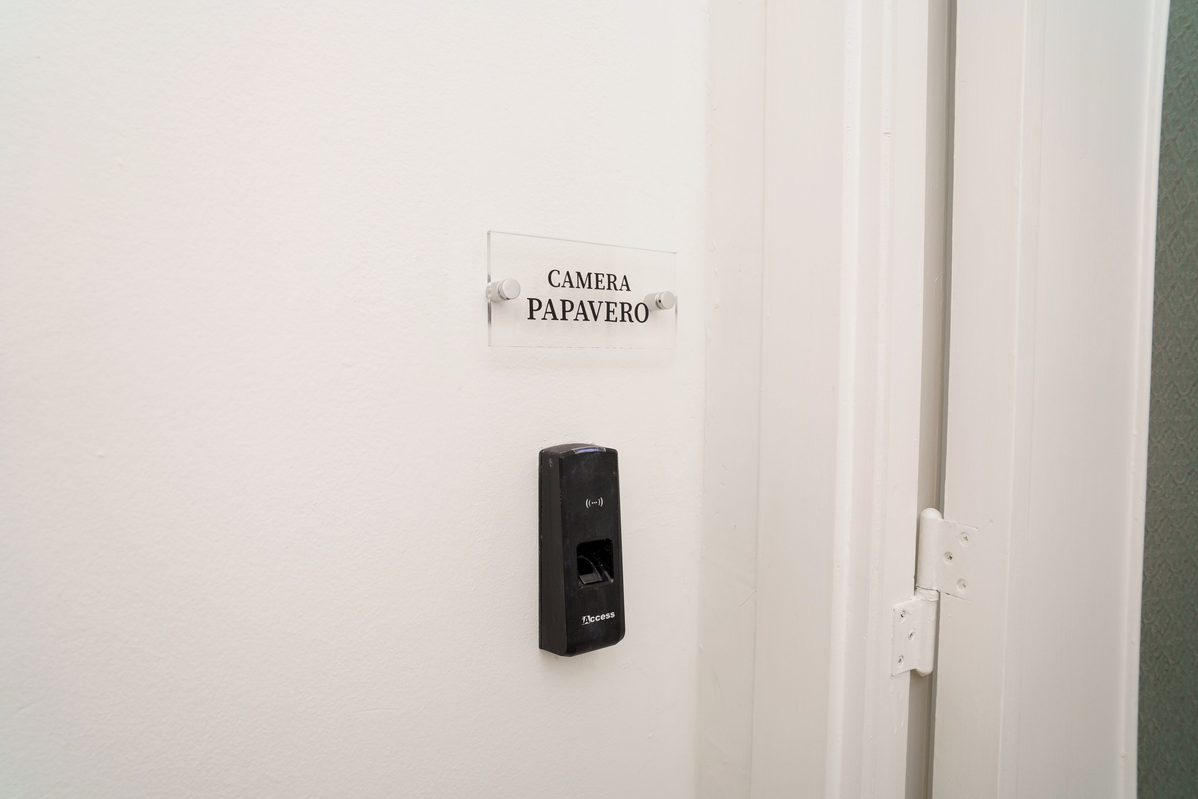 Una puerta blanca con un cartel que dice 'CAMERA PAPAVERO' y un portero automático negro en la pared.