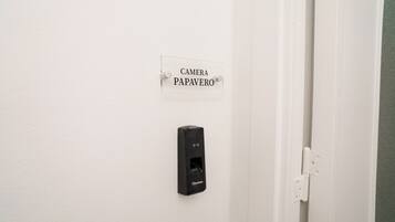 Una puerta blanca con un cartel que dice 'CAMERA PAPAVERO' y un portero automático negro en la pared.