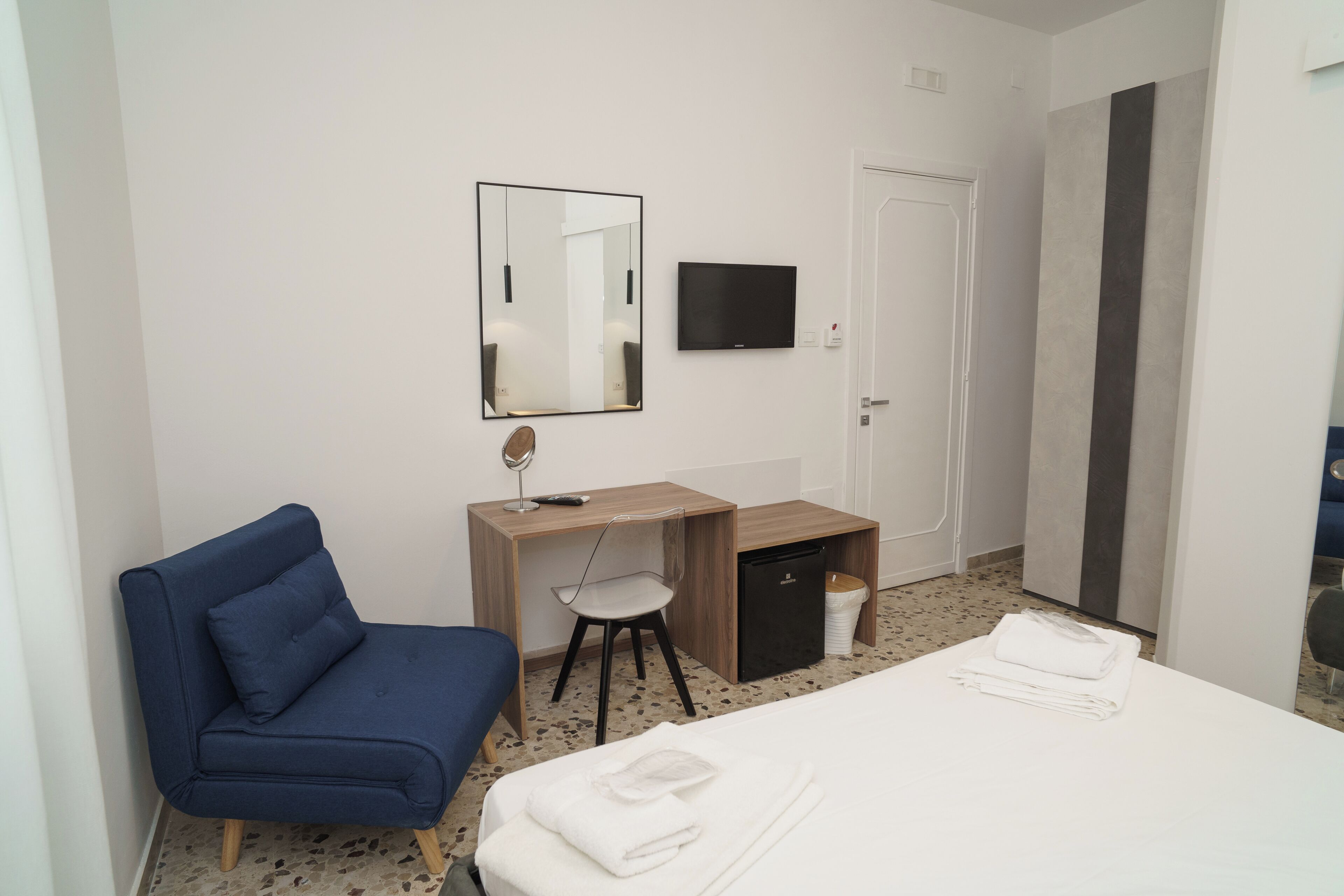 A hotel room with a bed, a desk, a chair, a television, and a wardrobe.