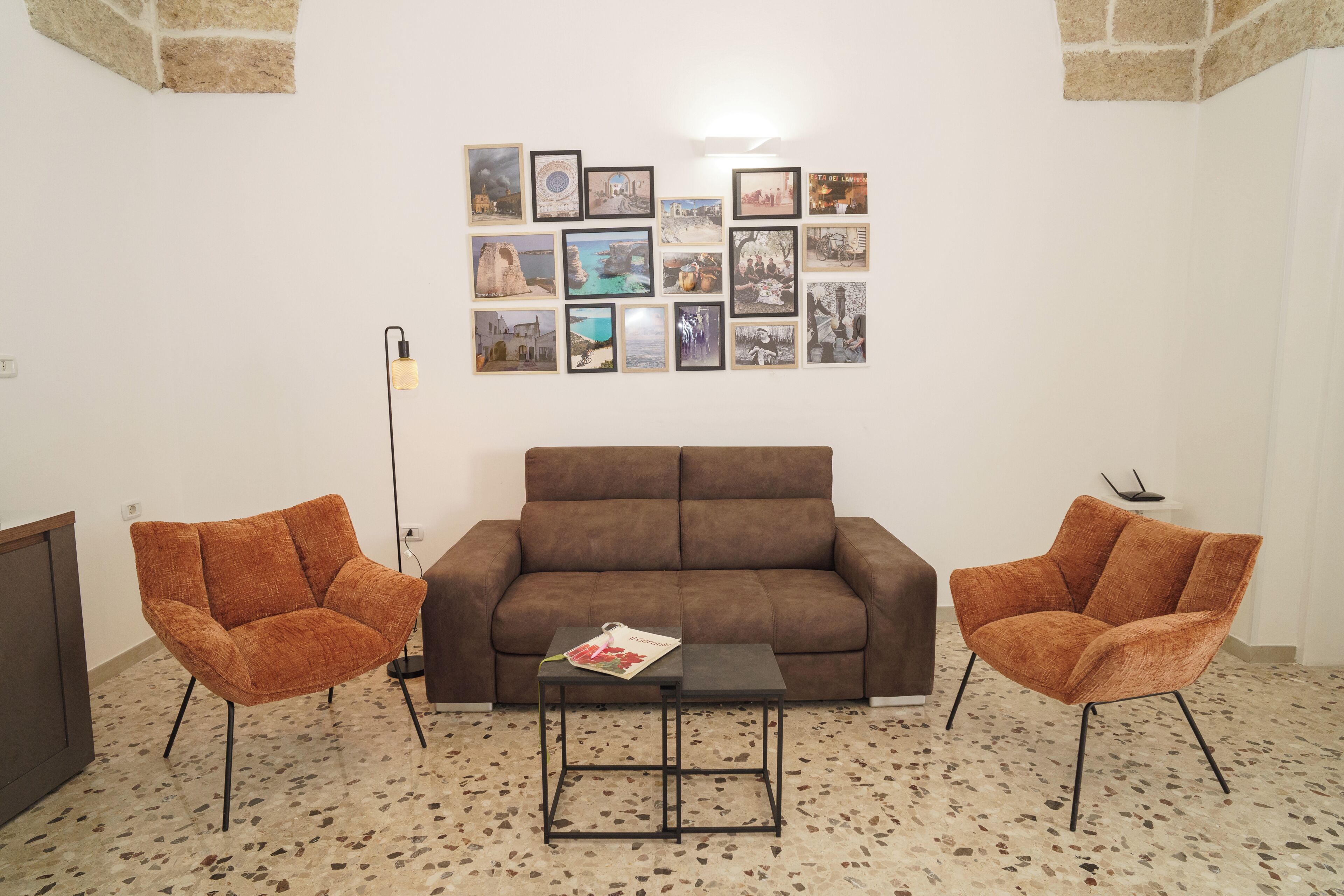 A living room with a brown sofa, two orange armchairs, a coffee table, and a wall adorned with framed pictures.