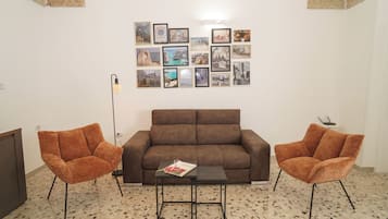 A living room with a brown sofa, two orange armchairs, a coffee table, and a wall adorned with framed pictures.