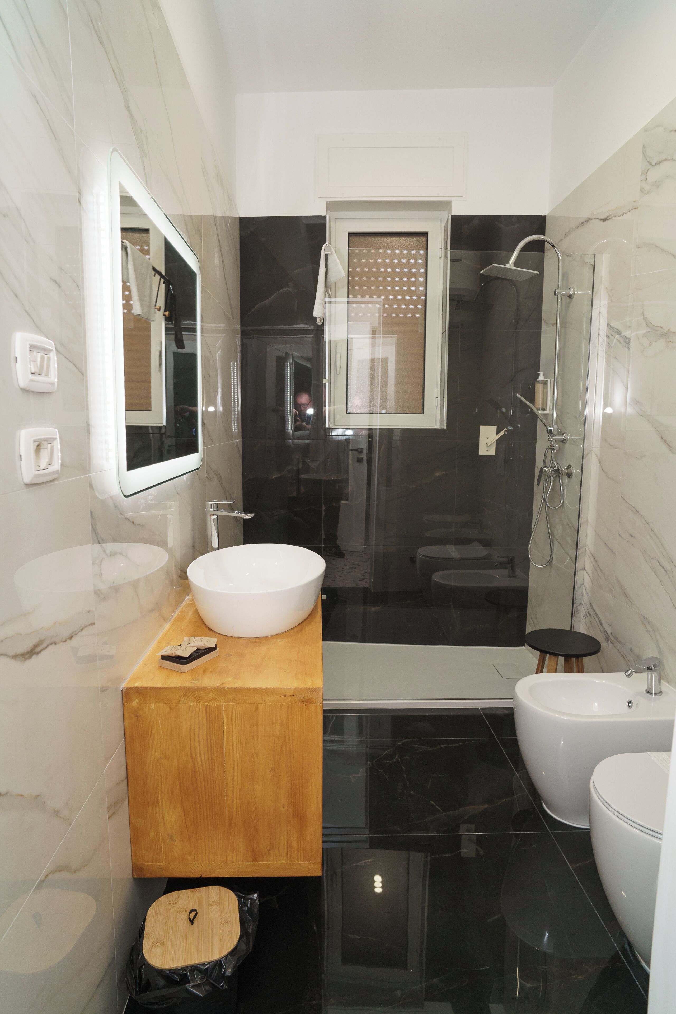 A modern bathroom with a large mirror, a wooden vanity, a white sink, a black bathtub, and a separate toilet.