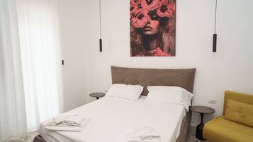 Habitación de hotel con cama, dos mesitas de noche, un sillón amarillo y una obra de arte grande en la pared.