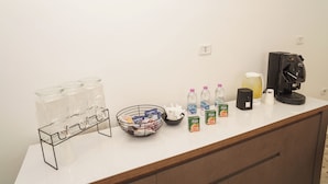 Un comptoir équipé d’une machine à café, de bouteilles d’eau, d’un bol de collations et d’un distributeur de boissons en verre.