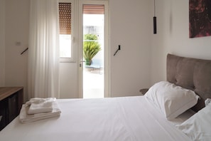 A bedroom with a bed, a nightstand, a window with blinds, and a door leading to an outdoor area. - B&B Il Geranio (Calimera)
