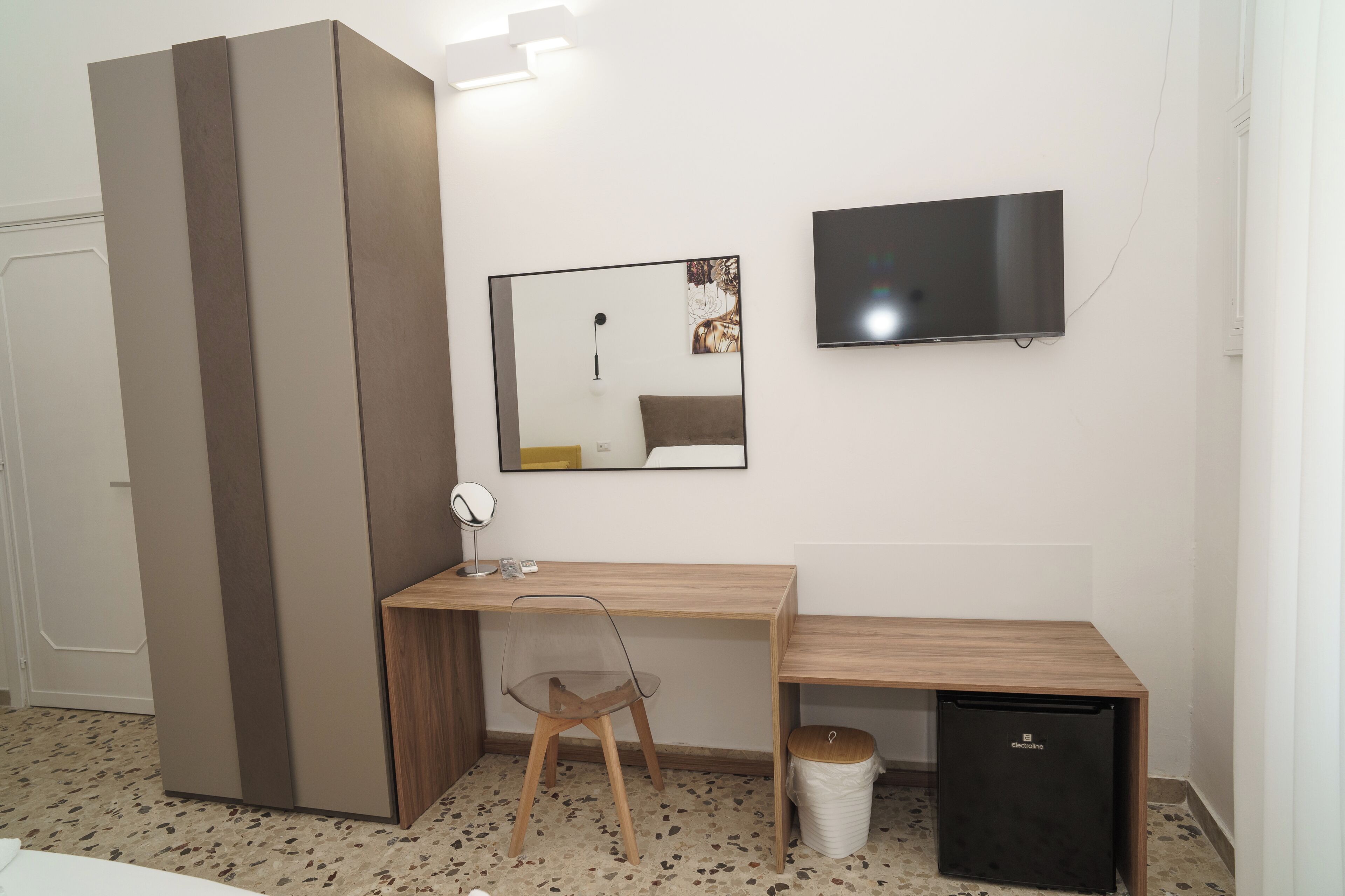 Habitación compacta con cama, escritorio, silla, televisor y un refrigerador pequeño.