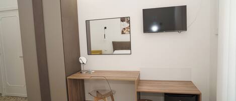 Habitación compacta con cama, escritorio, silla, televisor y un refrigerador pequeño.