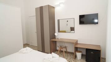 Une chambre d’hôtel équipée d’un lit, d’un bureau, d’une chaise, d’une télévision et d’un petit réfrigérateur.