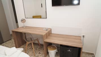 A hotel room with a wooden desk, a chair, a small trash bin, a mirror, and a television mounted on the wall.