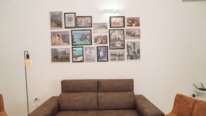 Une pièce avec un canapé marron, un lampadaire et un mur orné de divers portraits encadrés.