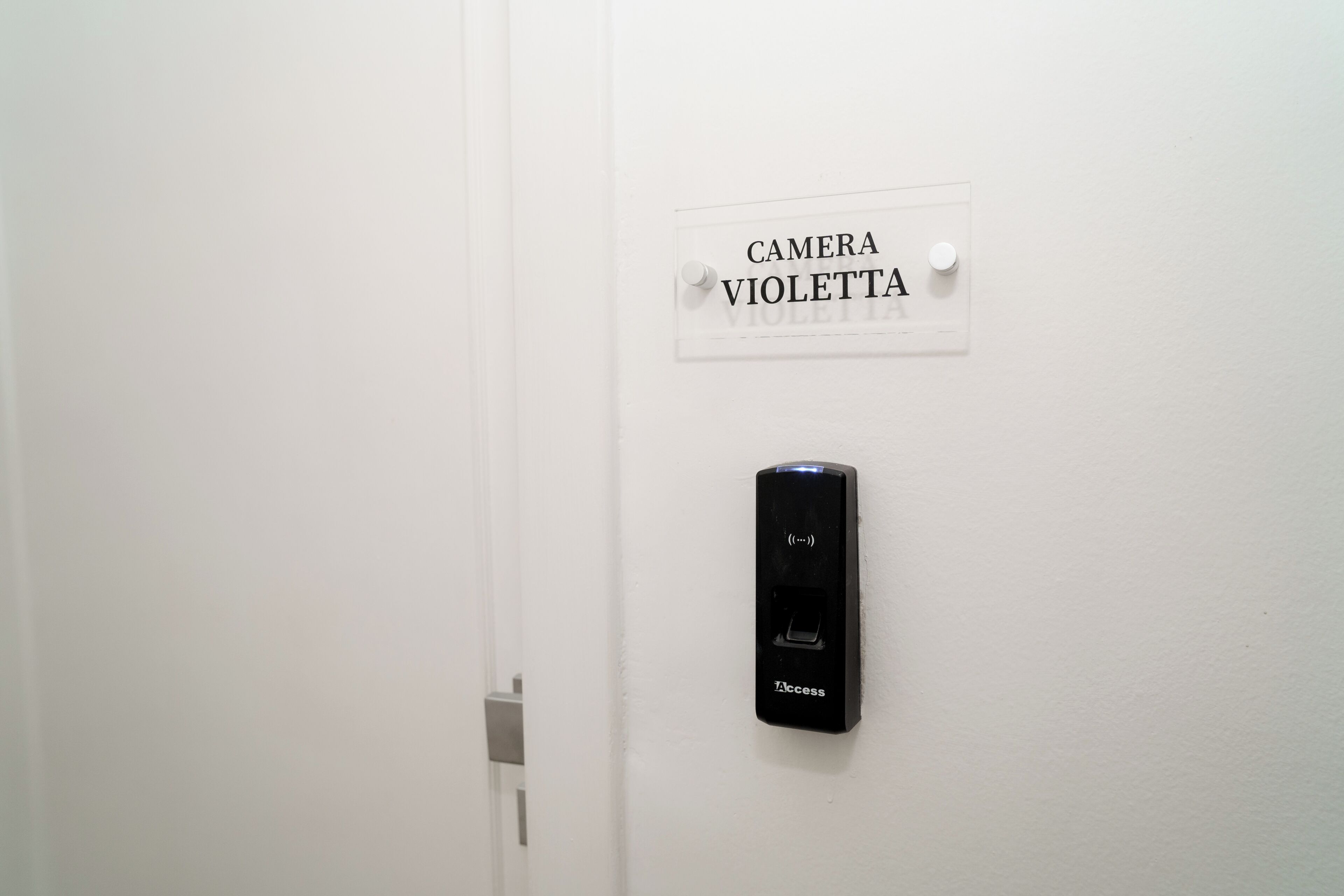 Una porta amb un senyal que diu 'CAMERA VIOLETTA' i un dispositiu d'intercomunicador negre muntat a la paret.