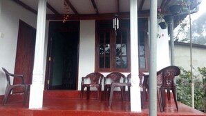 A covered porch with a red floor, white columns, and wooden beams. There are plastic chairs and a table. - St Clair Holiday Home (Nuwara Eliya)