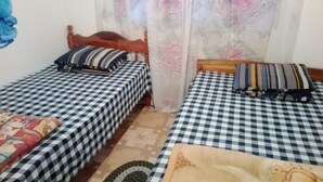 A room with two single beds, each with a checkered bedspread and pillows. There is a patterned curtain and a small rug on the floor. - St Clair Holiday Home (Nuwara Eliya)