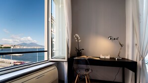 A room with a desk, chair, and a view of a body of water and a mountain. - Seaside Caracciolo (Naples)