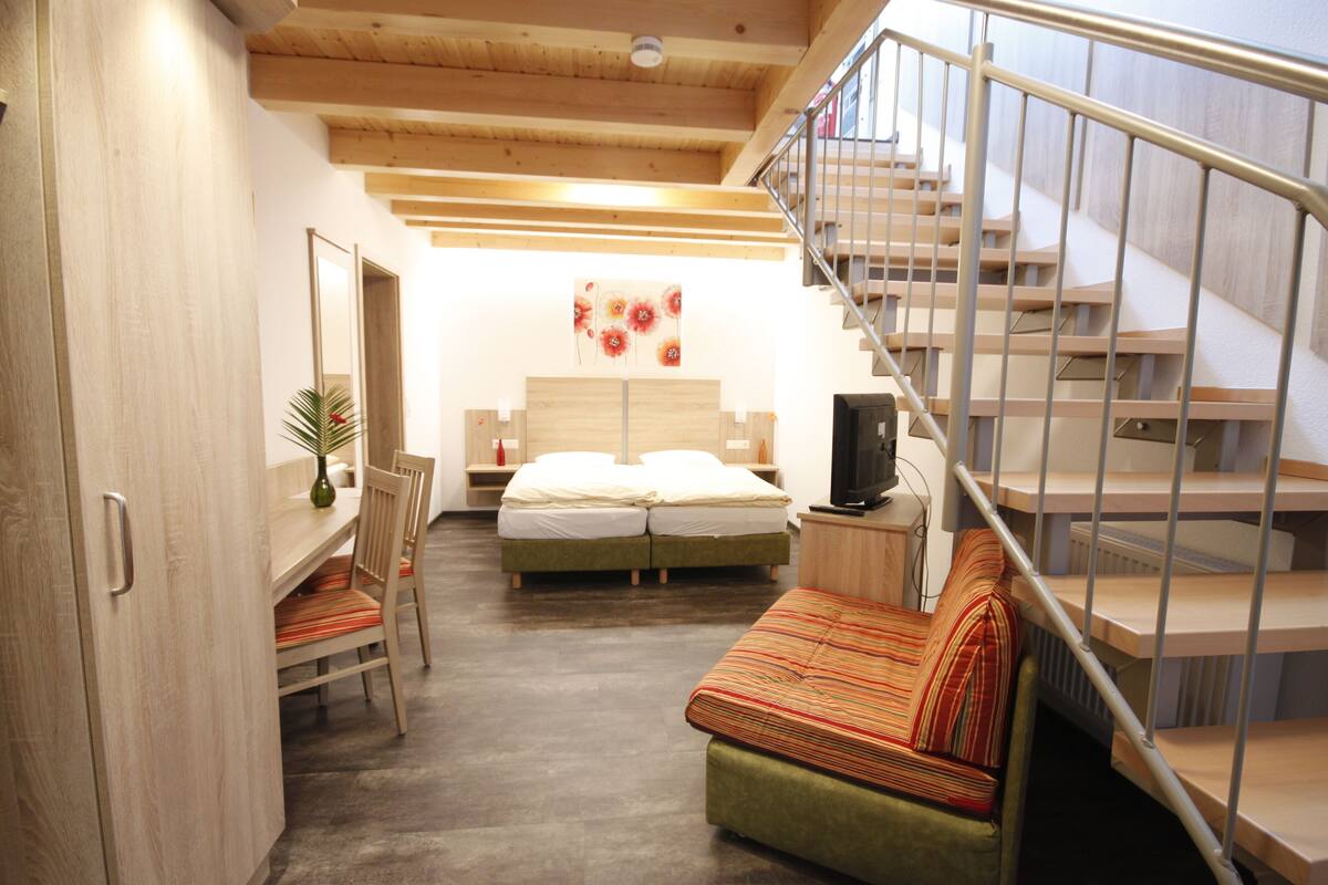 A compact bedroom with a bed, a sofa, a desk, and a staircase.