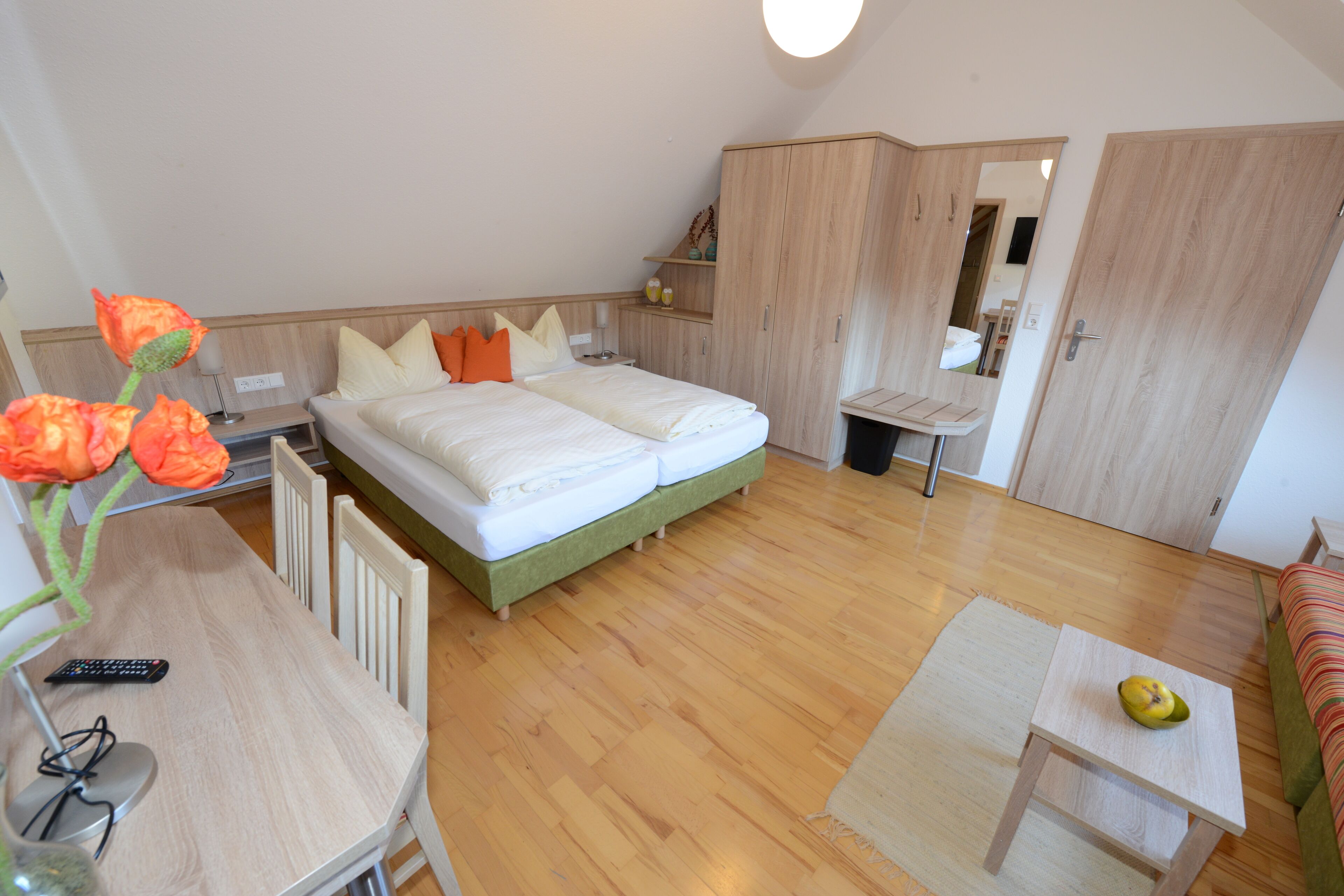 Un dormitorio con cama, escritorio, silla, una mesita con fruta y espejo.