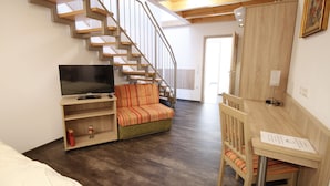 A room with a wooden staircase, a television on a wooden shelf, a sofa with striped cushions, and a wooden desk with a chair. - Am Treidelpfad (Hassmersheim)