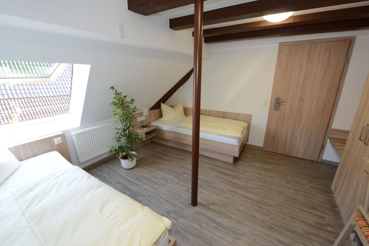 A bedroom with a bed, a small sofa, a potted plant, and a wooden wardrobe.